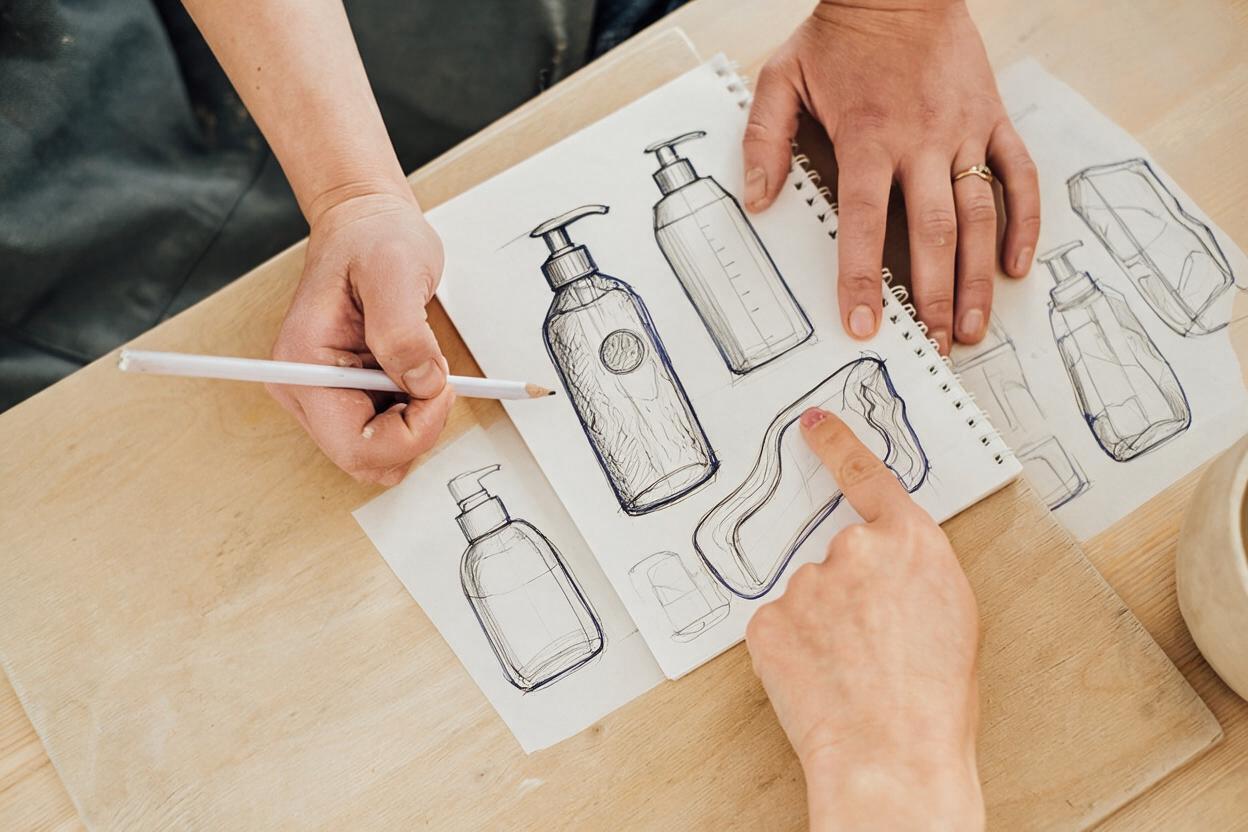Hands sketching premium shampoo bottle designs on paper